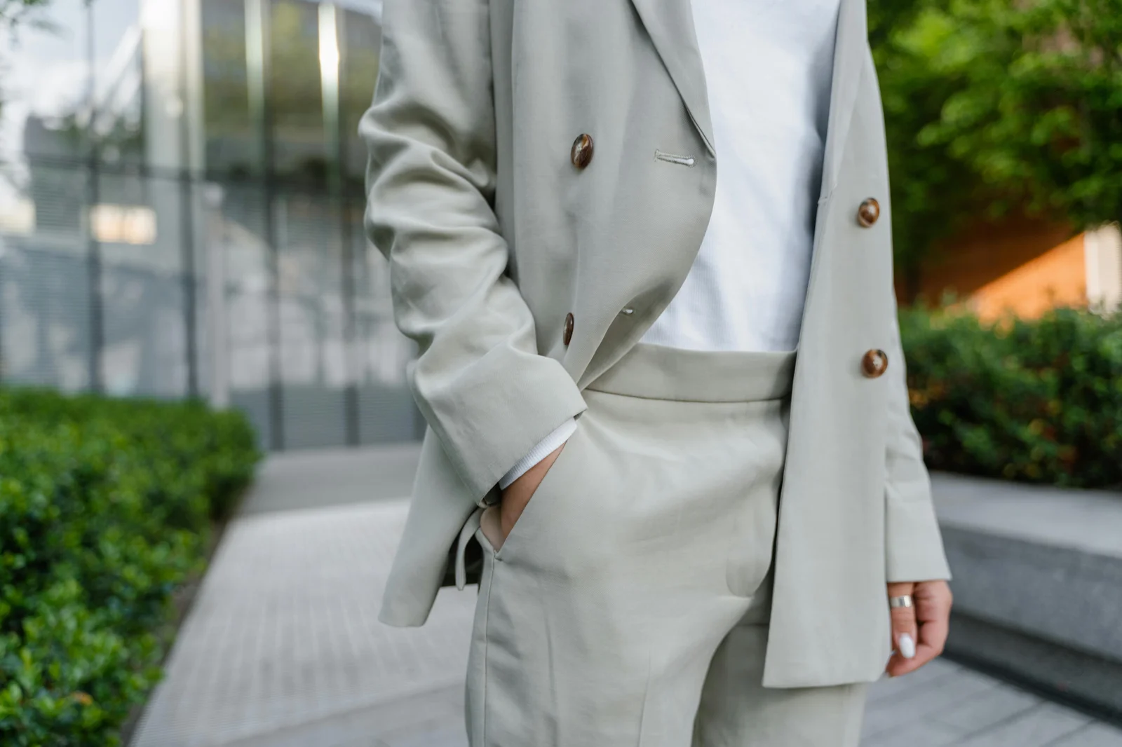 Persona con blazer beige y camisa blanca en exterior, estilo urbano y primaveral.